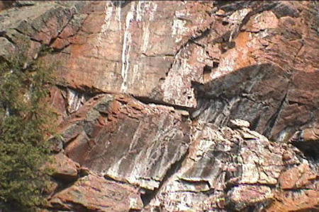 This is a close-up of the rock face showing the dull red iron stains, the brighter orange Xanthoria and white streaks of limestone eluted out of the rock. 	